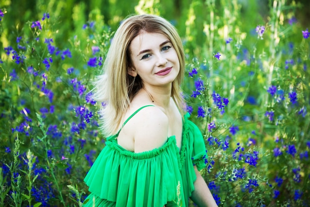 Blond european girl in a green dress  on nature with blue flowers