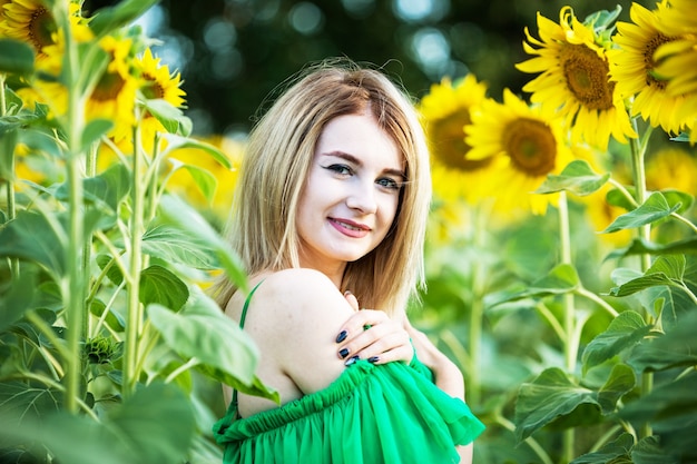 Ragazza europea bionda in un vestito verde sulla natura con i girasoli