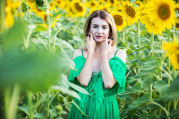 Ragazza europea bionda in un vestito verde sulla natura con i girasoli