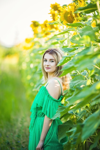 Blond european woman in a green dress on nature with sunflowers