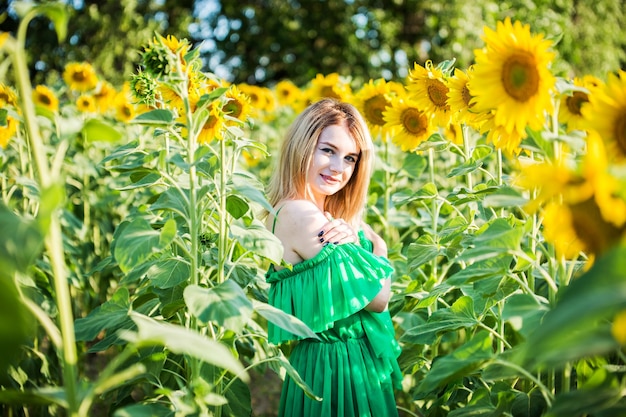 Blond Europees meisje in een groene jurk op aard met zonnebloemen