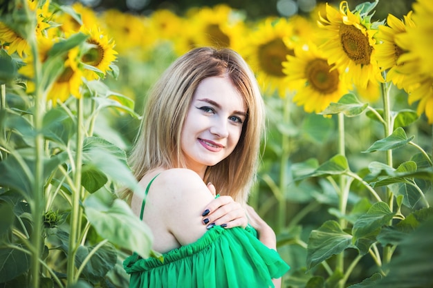 Blond europees meisje in een groene jurk op aard met zonnebloemen