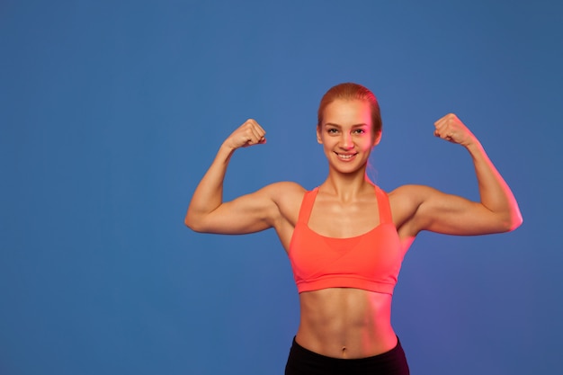 Blond female athlete showing biceps on blue background,