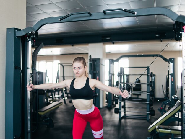 Blond fit woman doing exercise in crossover machine at gym