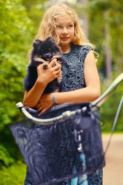 Blond girl on a bicycle holds a Spitz dog.