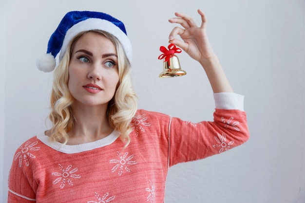 Blond girl in a Christmas hat with a bell in hands