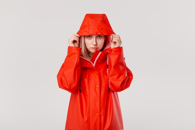 Blond girl puts on hood of a red raincoat, starting to rain.