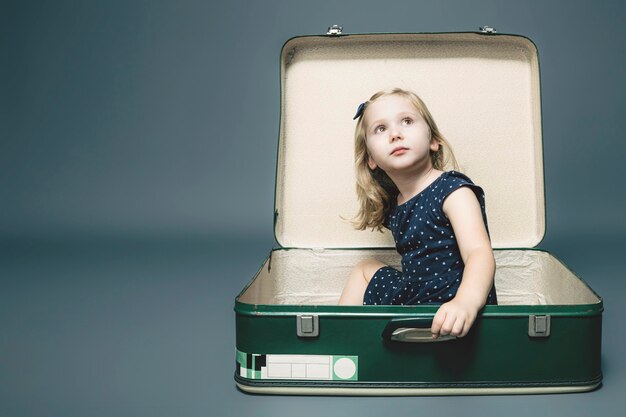 Blond girl sitting in a vintage suitcase. 