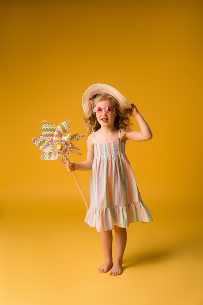 Blond girl smiling in sunglasses and summer sundress holding a windmill