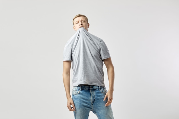 Blond guy dressed in a white tshirt and jeans stands on the white background