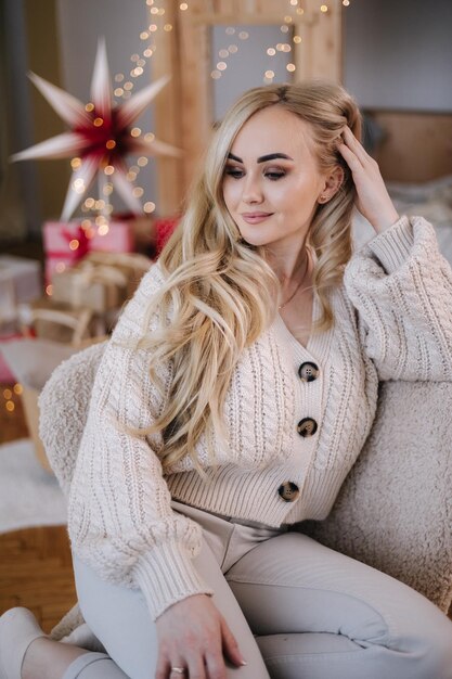 Blond haar vrouw in wit gebreid pak om thuis te zitten bij kerstboom mooie vrouw op vakantie