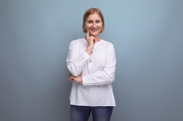 Blond hair woman of mature years in a white shirt smiling on a studio background