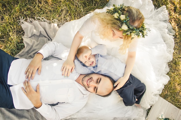 Blond haired toddler boy groom lying on knees of bride in wedding dress Outdoor wedding scene