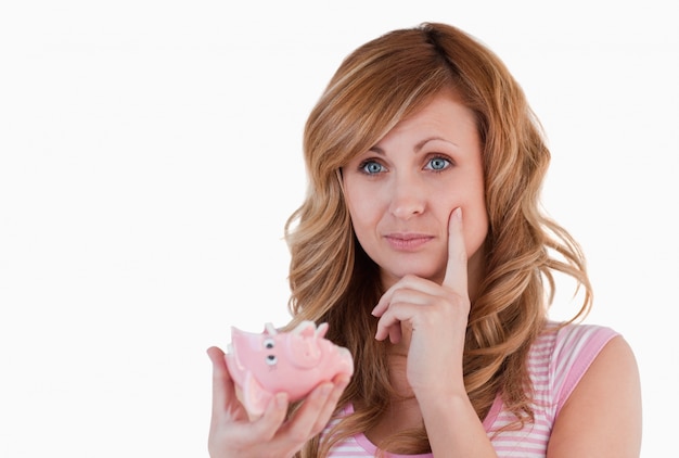 Blond-haired woman thoughtful while holding her broken piggybank