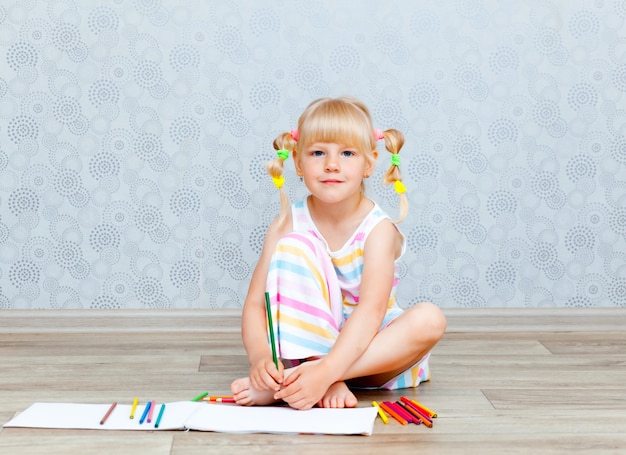 Foto la bambina felice bionda disegna sdraiata sul pavimento a casa. educazione della prima infanzia