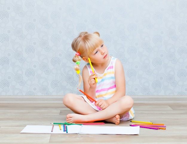 Фото Белокурая счастливая маленькая девочка рисует лежа на полу у себя дома. дошкольное образование