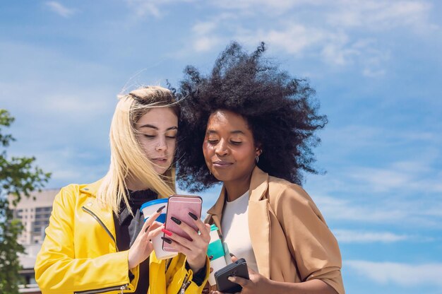 blond jong meisje toont telefoonscherm aan haar donkerbruine jonge vriend met afro