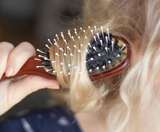 blond kamt nat en verward haar Jonge vrouw kamt haar verwarde haar na het douchen