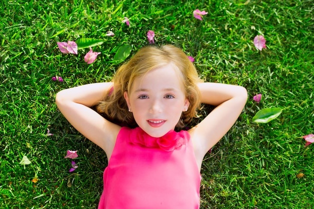 Photo blond kid girl lying on garden grass smiling aerial view