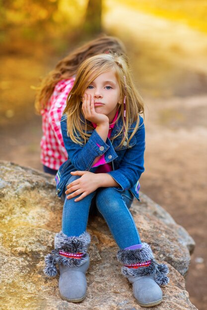 Ragazza bionda del bambino pensierosa annoiata nella foresta all'aperto