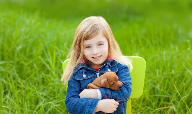 Blond kid girl with puppy pet dog in green grass