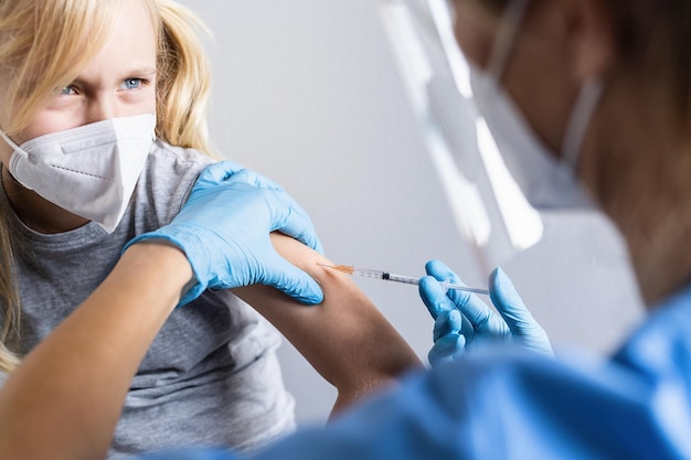 Blond kindmeisje kijkt naar de dokter met spuit in de hand en weigert spuit met vaccin terwijl ze wordt gevaccineerd of een injectie krijgt tijdens covid19 pandemie