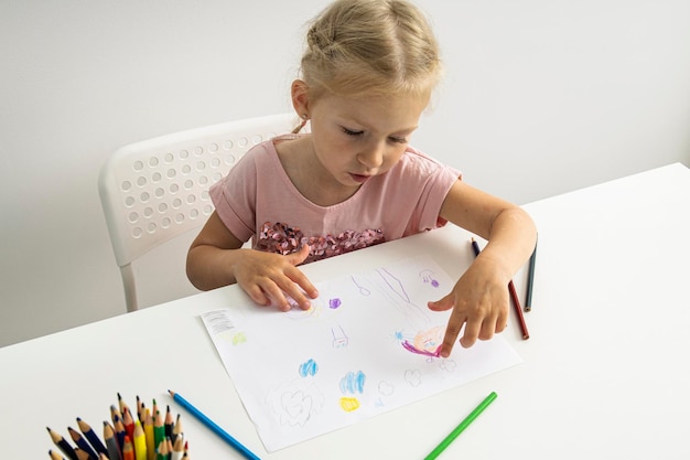 Blond kindmeisje tekent met kleurpotloden aan tafel