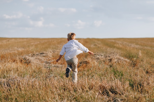 Ragazzino biondo che gioca fieno nel campo. estate, tempo soleggiato, agricoltura.