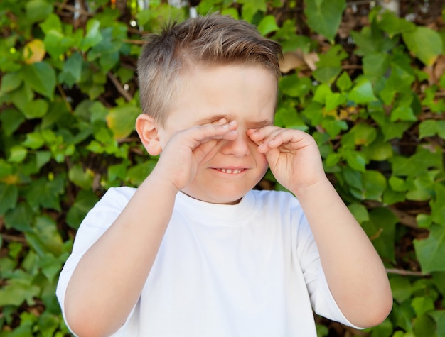 Белокурый маленький мальчик протирает глаза от аллергии
