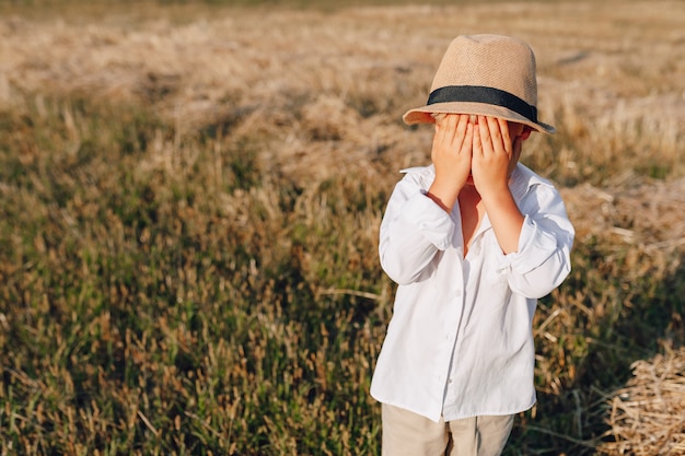 刈られた干し草のフィールドで遊ぶ麦わら帽子の金髪の少年。夏、晴天、農業。幸せな子供時代。