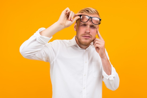 Blond man dressed in a classic white shirt squints at taking off his glasses onyellow