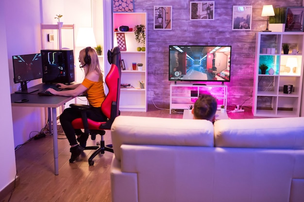 Blond meisje dat schietspellen speelt in een kamer met neonlicht. Gamer meisje op gaming stoel.