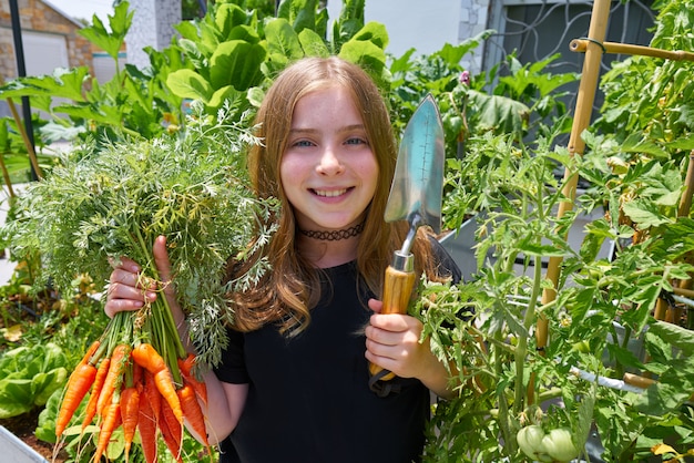 Blond meisje die wortelen stedelijke boomgaard oogsten