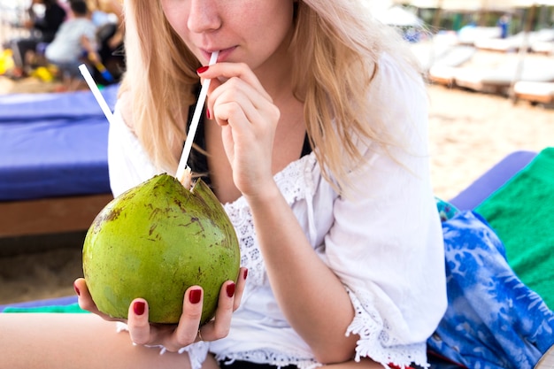 Blond meisje drinkt uit een kokosnoot op het strand