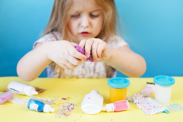 Blond meisje houdt paars slijm geïsoleerd op blauwe achtergrond kind spelen met slijm speelgoed