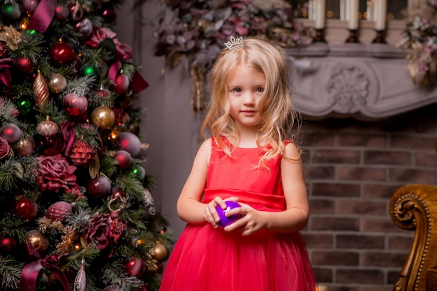 blond meisje in avond rode jurk in de buurt van de kerstboom