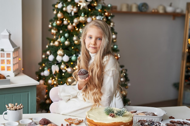 blond meisje in de keuken van het nieuwe jaar met cupcakes en snoep