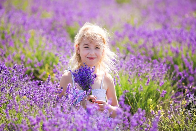 Blond meisje in de kleur jurk in het veld od lavendel met een kleine bouqet in haar handen