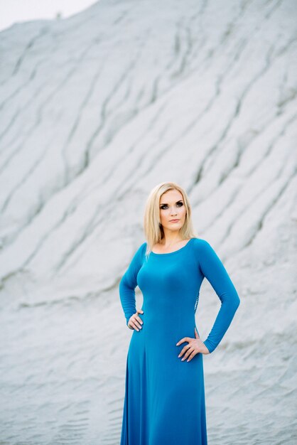 Blond meisje in een blauwe jurk met blauwe ogen in een granietgroeve tegen de achtergrond van grind