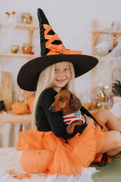 blond meisje in een heksenkostuum oranje gezwollen rok houdt een dwerg teckel op schoot Halloween