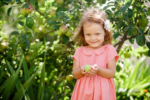 Blond meisje in een roze jurk met een appel in haar handen in de tuin