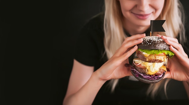 Blond meisje in een zwart T-shirt met een grote zwarte burger in haar handen