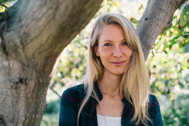 Foto blond meisje in haar dertiger jaren poseert glimlachend in een tuin voor een paar bomen