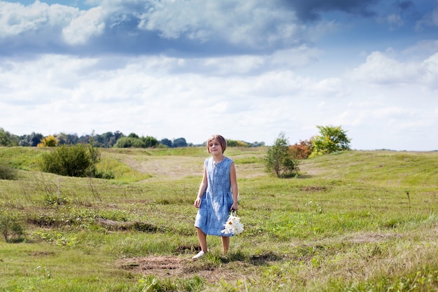 Blond meisje in jurk met boeket van madeliefjes in zomer veld