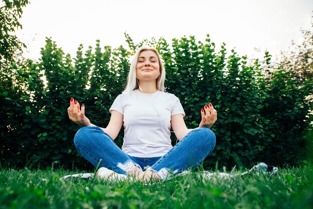 Blond meisje in koptelefoon zit in meditatieve pose luisteren naar muziek op groen gras