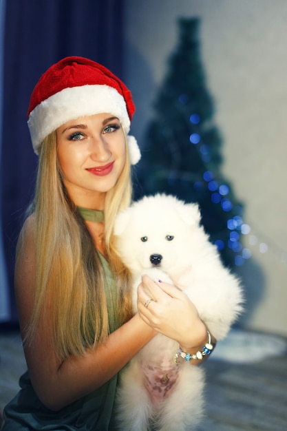 Blond meisje in rode kerstmuts met Samojeed husky hond in kerstversiering