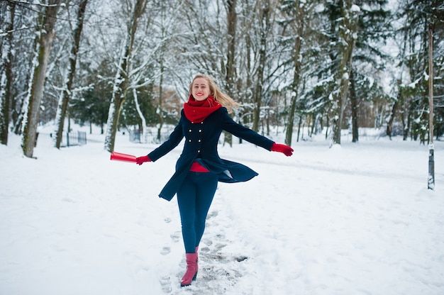 Blond meisje in rode sjaal en jas wandelen in het park op winterdag.