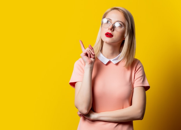 Blond meisje in roze jurk en bril op gele achtergrond