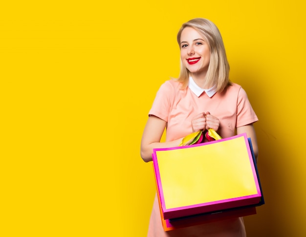 Blond meisje in roze jurk met boodschappentassen op gele ruimte