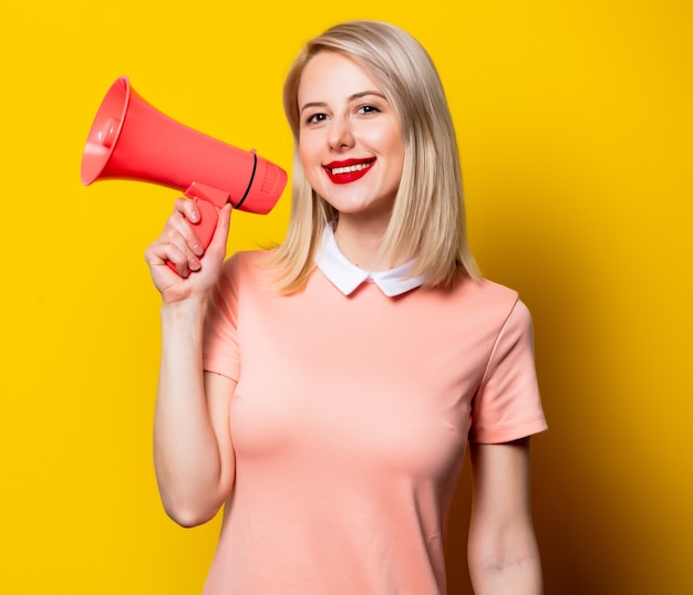 Blond meisje in roze jurk met megafoon op gele achtergrond